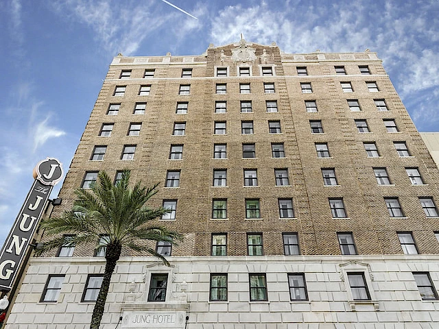 A large brick and stone hotel building with a sign reading 'Jung Hotel' and a palm tree in front.